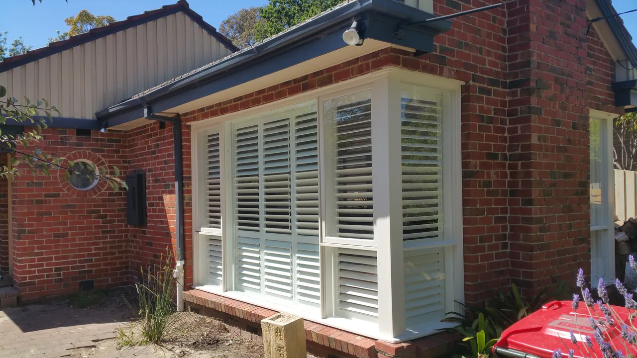 Plantation shutters fitted inside a bay window, seen from outside