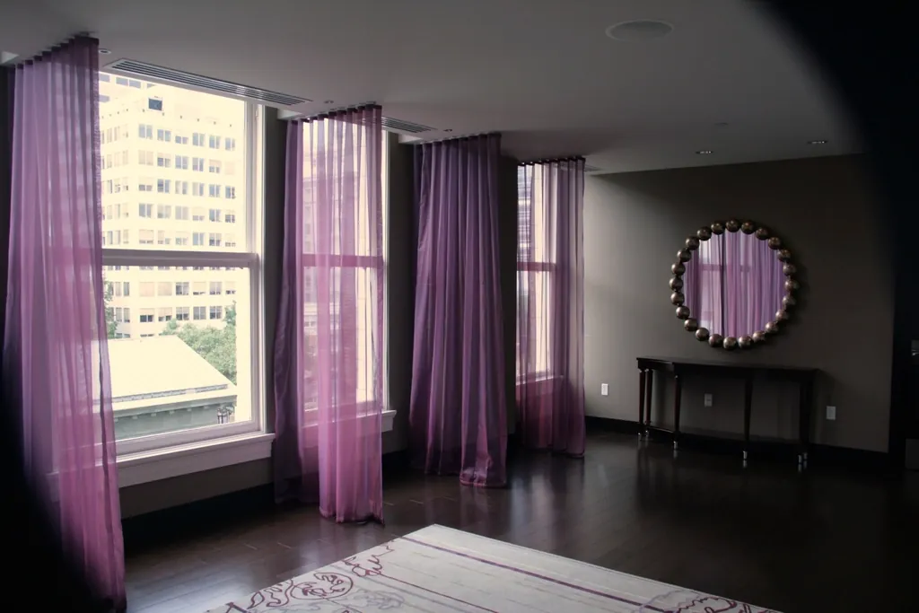 Violet sheer panels framing tall windows in a city living room